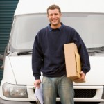 Delivery person standing with van holding clipboard and box