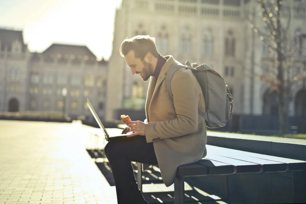 A man smiling and working on his laptop outdoors.