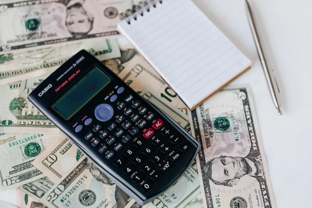 A calculator with a notebook and a pen and stack of money