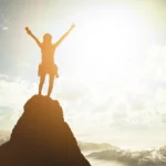 Person celebrating on mountain peak signifying success