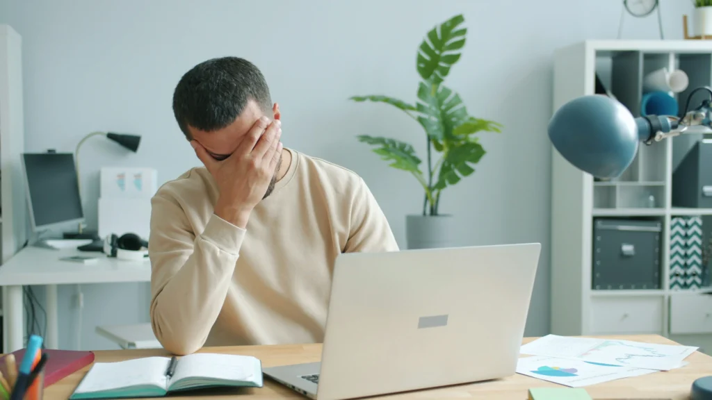A person holding their head in frustration while working on their laptop at an office desk.